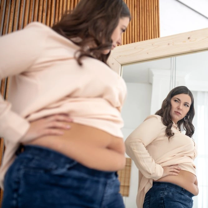 mulher com grande barriga para fora da blusa olhando-se no espelho